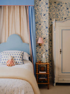 Bedroom with blue headboard, floral wallpaper, and wooden nightstand.