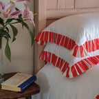 Red and white striped pillows on a bed with a vase of flowers and book on a side table.