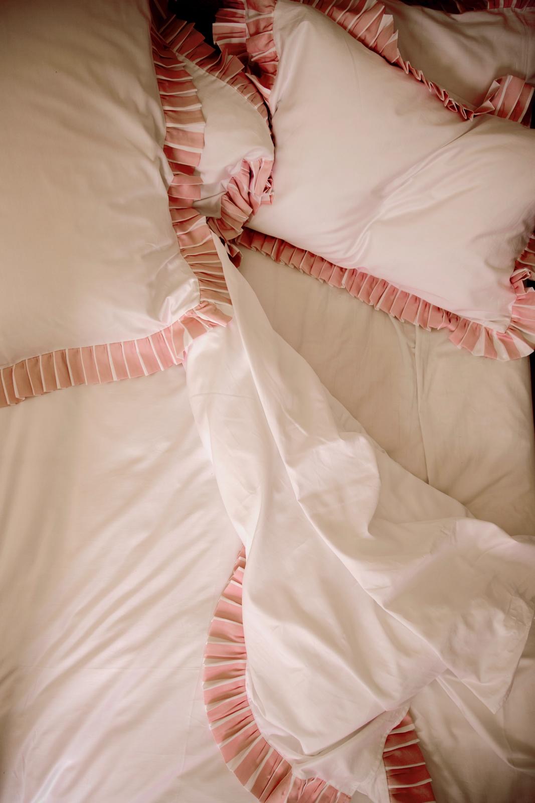 Close-up of a white duvet cover with pink and white marshmallow trim on a bed. signature sukun red logo