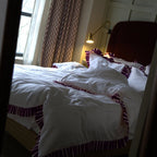 Bedroom with a bed covered in white bedding and decorative pillows, next to a window with curtains.