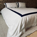 White quilt with navy border on a bed against a brick wall. border in navy blue