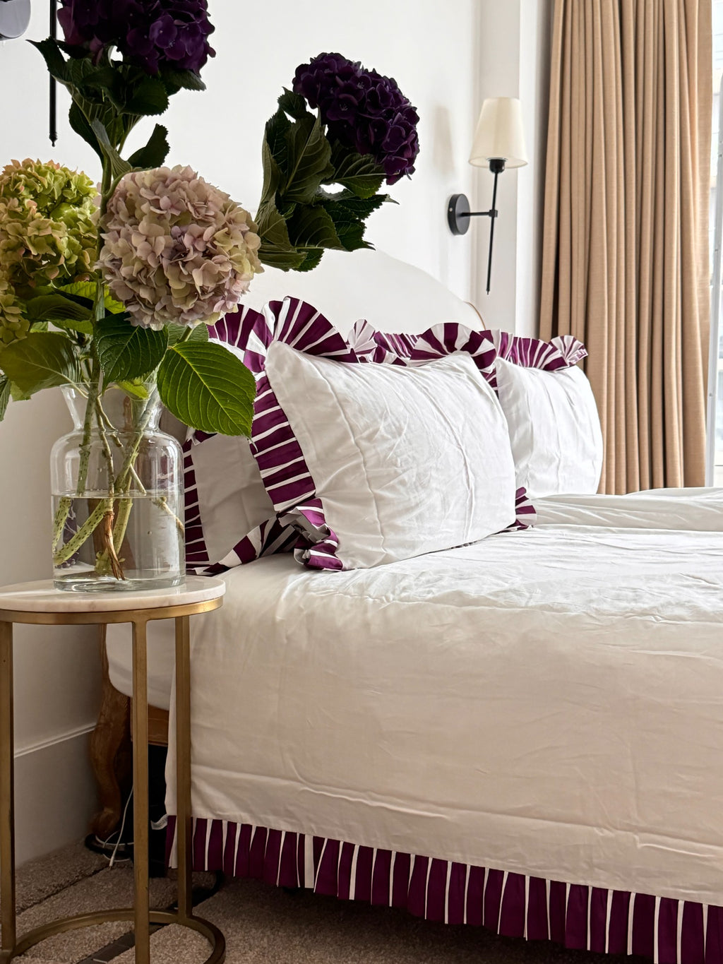 Neatly made bed with decorative pillows and a vase of flowers on a side table.